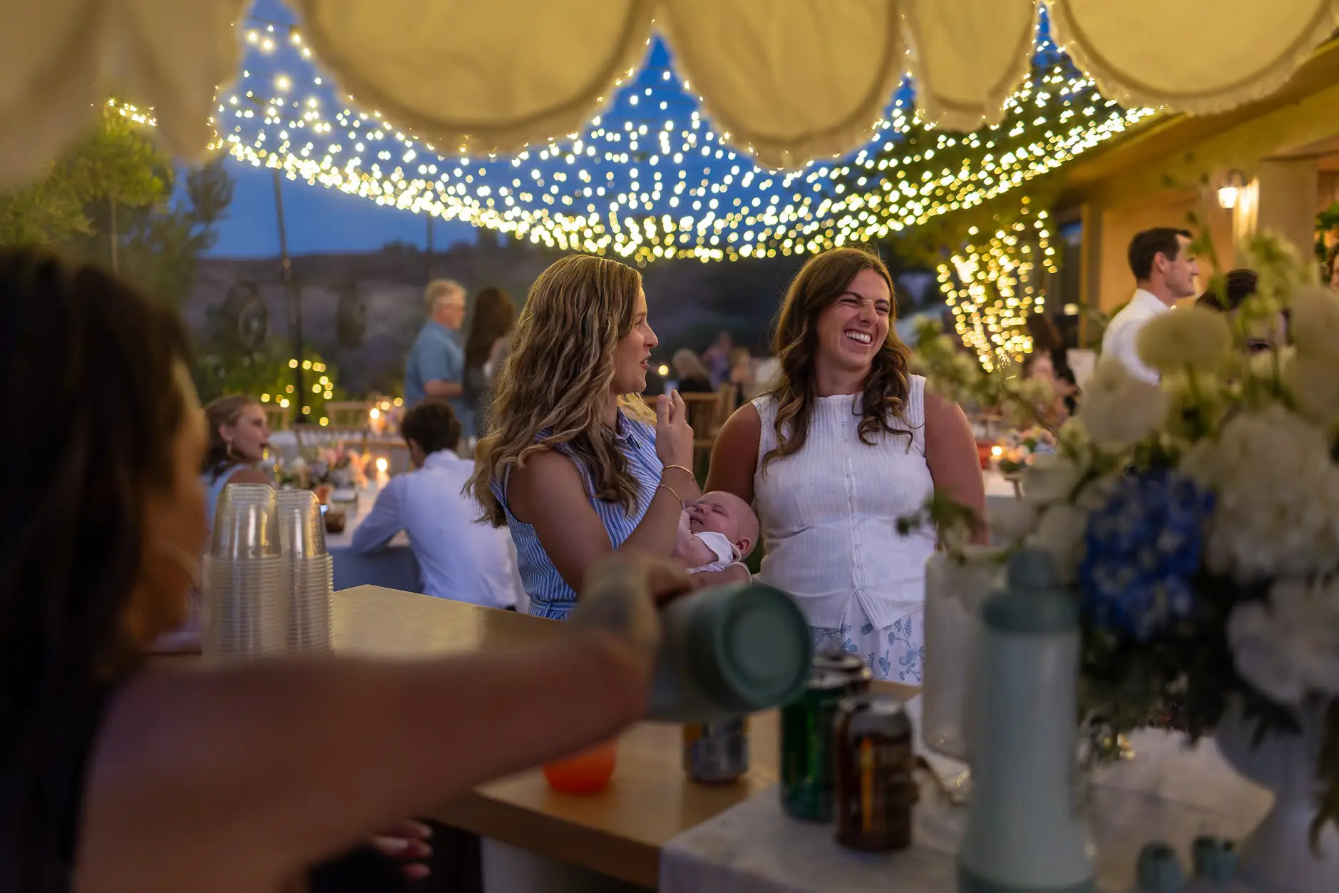 Guests laughing under canopy string lights at a twilight wedding celebration in Redlands, California